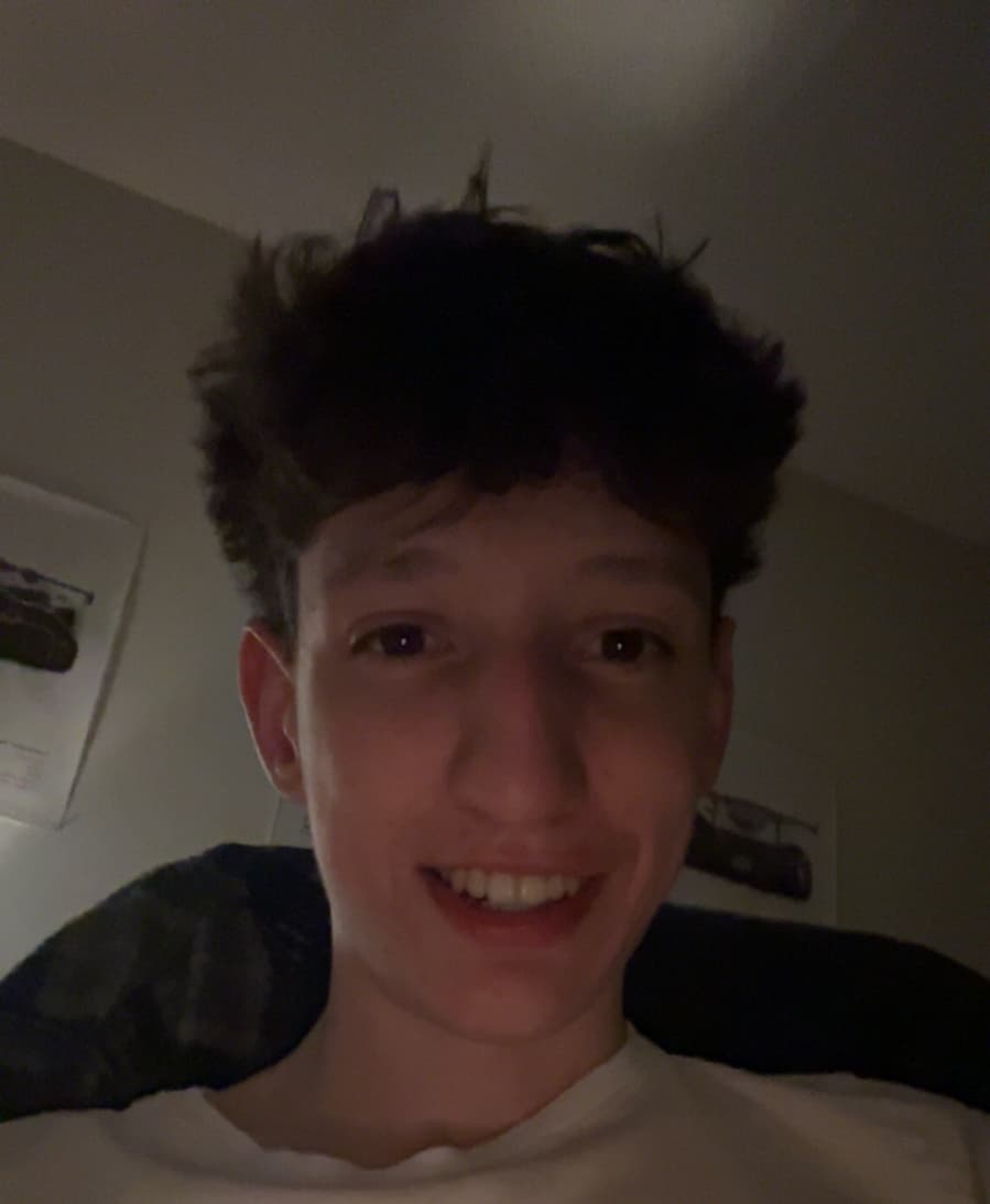 Smiling young man with dark messy hair in a white shirt in a dim room.